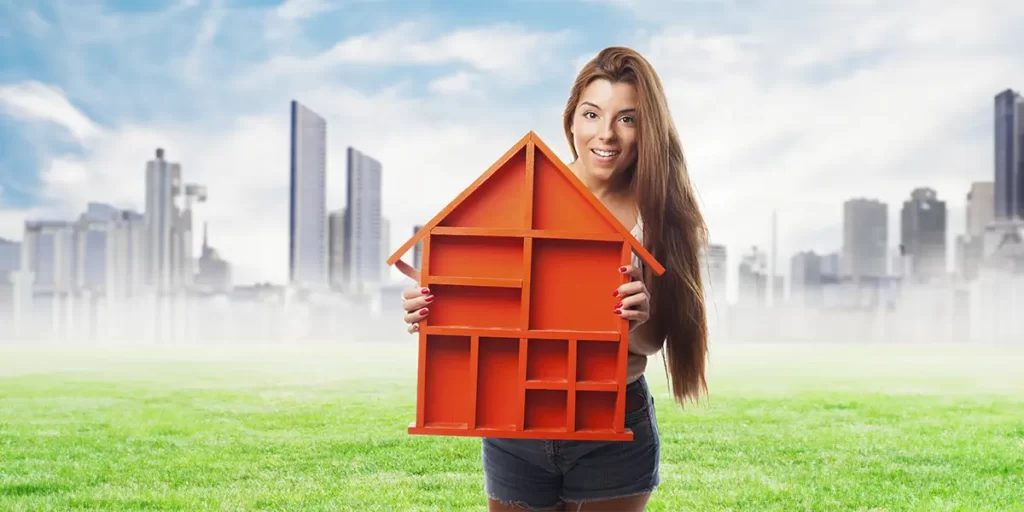 anúncios para lançamento imobiliário anúncios para lançamento imobiliário: A imagem mostra uma jovem sorridente segurando uma estrutura que parece ser uma casa em miniatura, de cor laranja. Ela está de pé em um ambiente ao ar livre, com um céu azul parcialmente nublado ao fundo. Ao fundo, há uma cena urbana com edifícios altos, sugerindo que a cena pode estar acontecendo em uma área perto de uma cidade. A jovem está vestida com calça curta e parece estar em um ambiente ao ar livre, possivelmente um parque ou uma área de lazer, com grama verde ao redor. A imagem tem um estilo de fotografia com um filtro que dá uma sensação de ilusão ou representação artística.