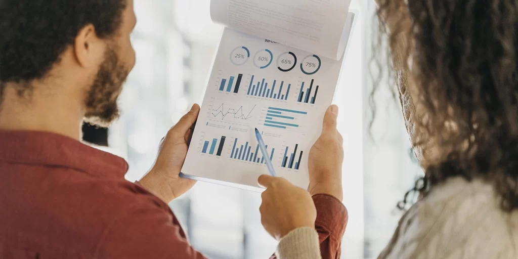 indicadores de desempenho indicadores de desempenho: imagem de duas pessoas de costas olhando para um papel com vários gráficos.