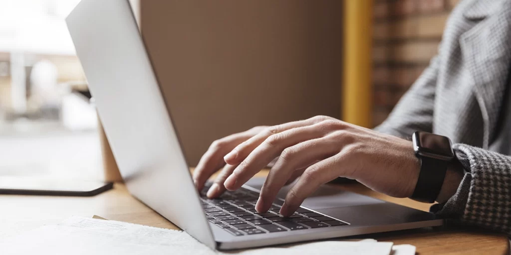 Marketing de conteúdo para construtoras Marketing de conteúdo para construtoras: A imagem mostra uma pessoa sentada em frente a um laptop aberto. A pessoa está usando um teclado externo. Ela está vestindo uma camisa com um padrão que parece ser um terno ou uma jaqueta de tecido, o que pode indicar um ambiente profissional ou acadêmico. A mão da pessoa está sobre o teclado, e ela parece estar digitando ou segurando o teclado. Há uma página de papel aberta ao lado do laptop, mas não é possível ler o conteúdo. A foto foi tirada de cima, focando na mão e no teclado, e a cena está desfocada para enfatizar a atividade da mão. A luz natural parece estar iluminando a cena, sugerindo que a foto foi tirada durante o dia.