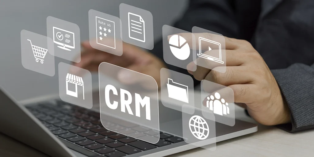 CRM para construtoras CRM para construtoras: close nas mãos de uma pessoa digitando num notebook. Em destaque alguns ícone que representam CRM.
