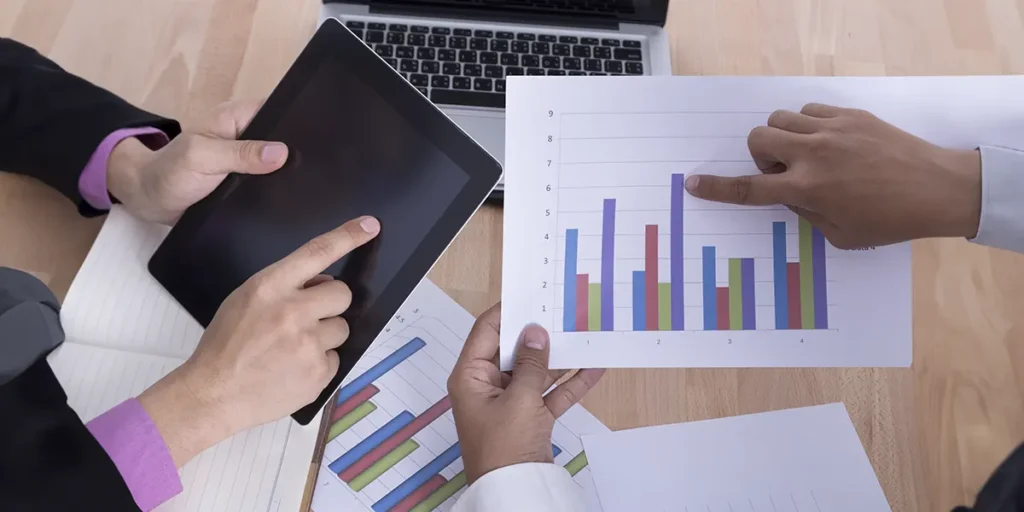 Relatórios de vendas de incorporadoras: a imagem apresenta as mãos de duas pessoas, uma segurando um tablet e a outra segurando um papel com um gráfico, apontando para os dados.
