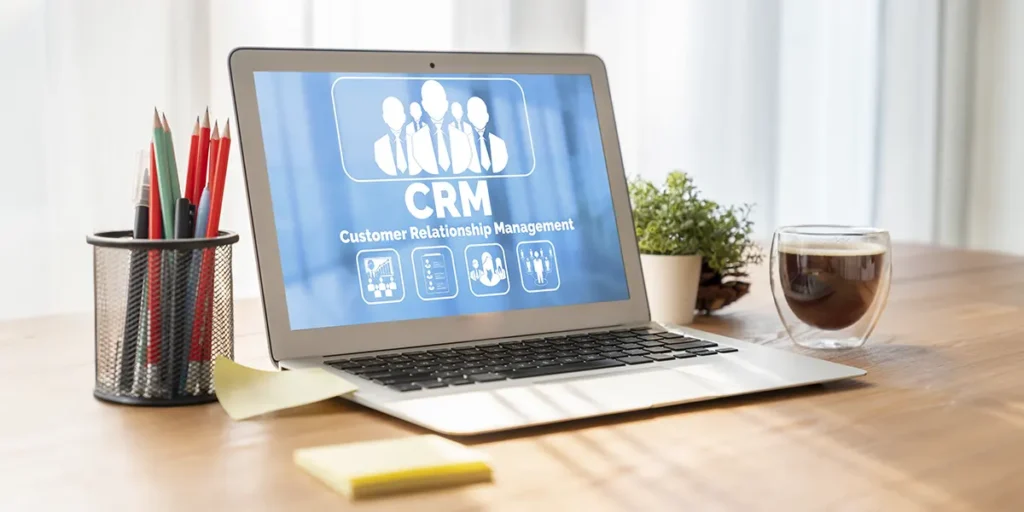 Relatórios de vendas de incorporadoras: a imagem apresenta um notebook aberto com um plano de fundo escrito CRM. Ao lado do notebook, um porta lápis com alguns lápis coloridos e do outro, uma xícara com café.