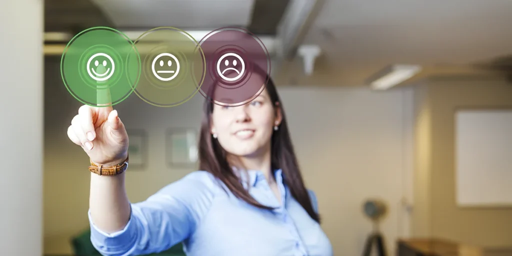 potenciais clientes A imagem mostra uma mulher em uma bata de trabalho segurando um celular com interface virtual com várias expressões faciais. A mulher está olhando para a tela com uma expressão neutra. O fundo é um ambiente moderno com paredes brancas e janelas de vidro. A imagem está em foco e as cores são brilhantes e vibratos. A atmosfera geral da imagem é profissional e animada.