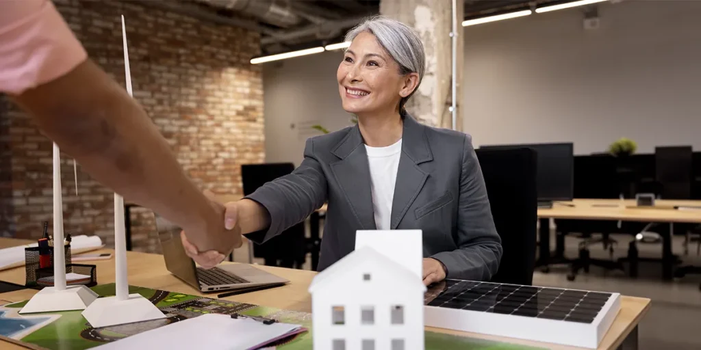 acompanhamento de transações de incorporadoras acompanhamento de transações de incorporadoras: mulher num escritório apertando a mão de outra pessoa e sorrindo.